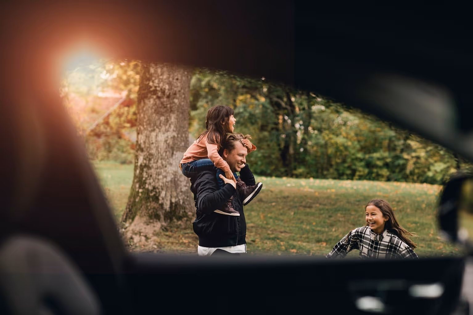 Man bär ett barn på axlarna medan en annan flicka springer och skrattar i en park.