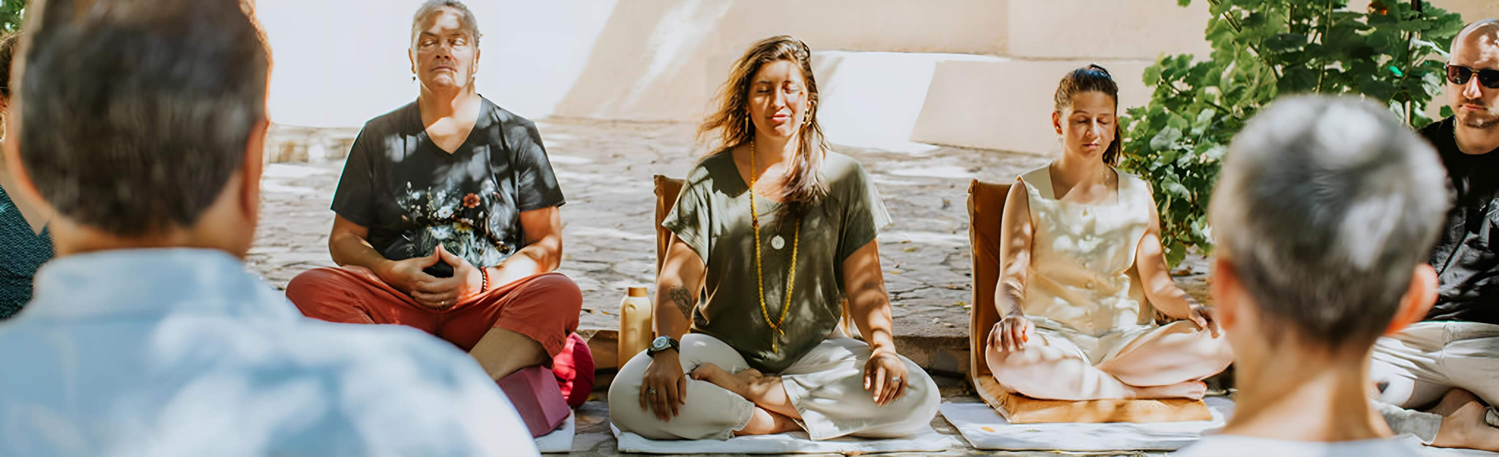 A diverse group of people sitting cross-legged outdoors, meditating with eyes closed.