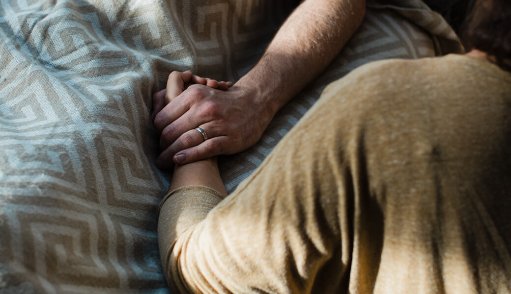 Two people holding hands over a patterned blanket, symbolizing comfort and connection.
