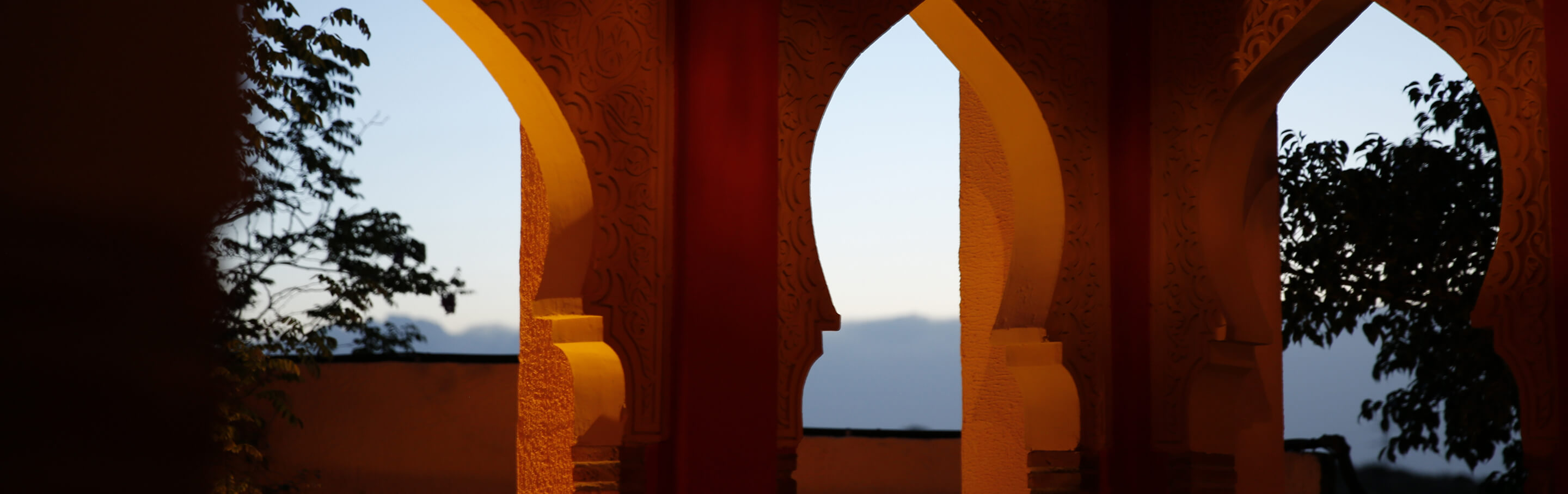 Ornate orange arches framing a twilight sky and silhouetted trees.