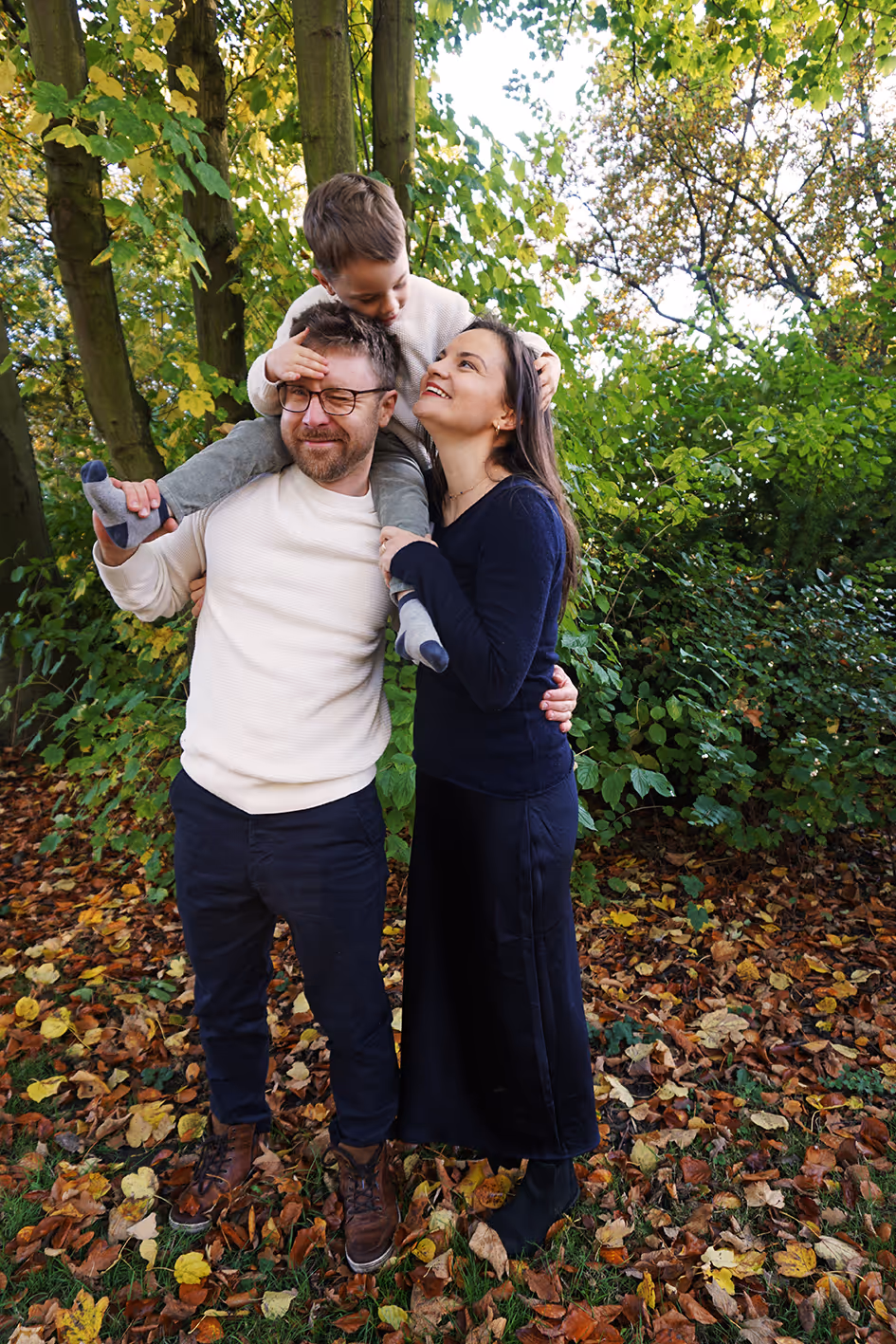 Junge Familie. Sohn sitzt auf Papas Schultern. Mama schaut zu ihm hoch.