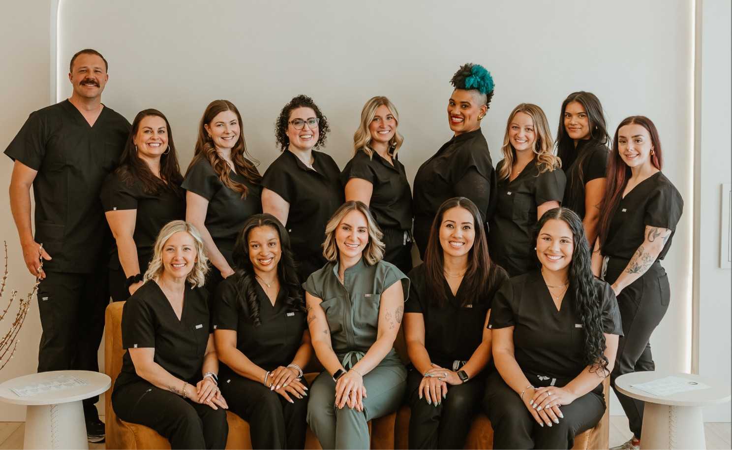 Group portrait of smiling healthcare professionals in black and gray scrubs posing indoors.