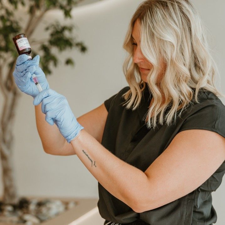 Blonde woman wearing blue gloves draws liquid from a vial with a syringe.