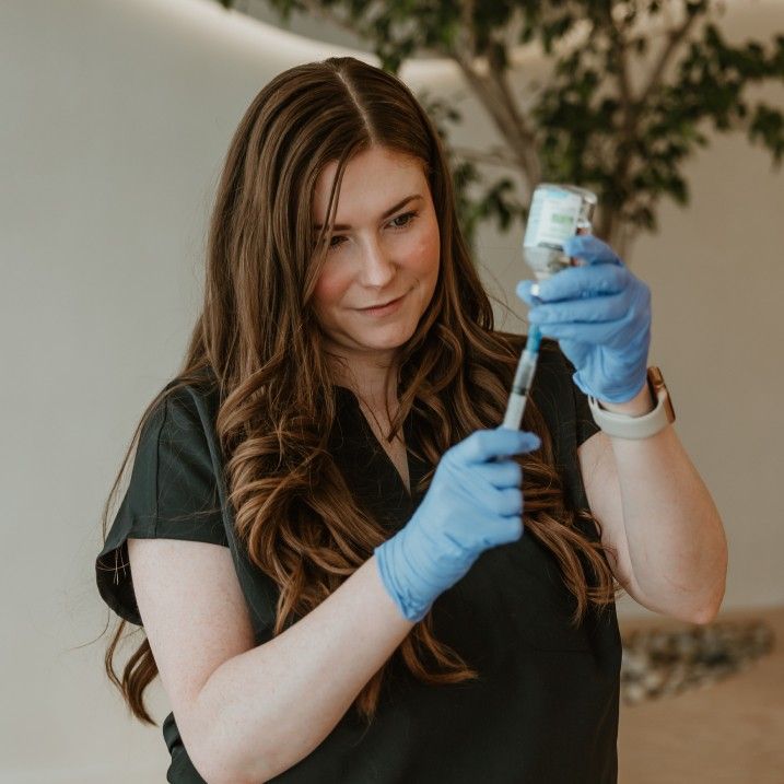 Woman wearing blue gloves drawing liquid from a vial into a syringe.