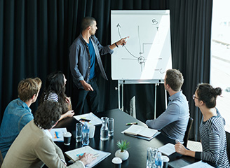 Businessman presenting a strategy diagram on a flip chart to a diverse team seated around a conference table.