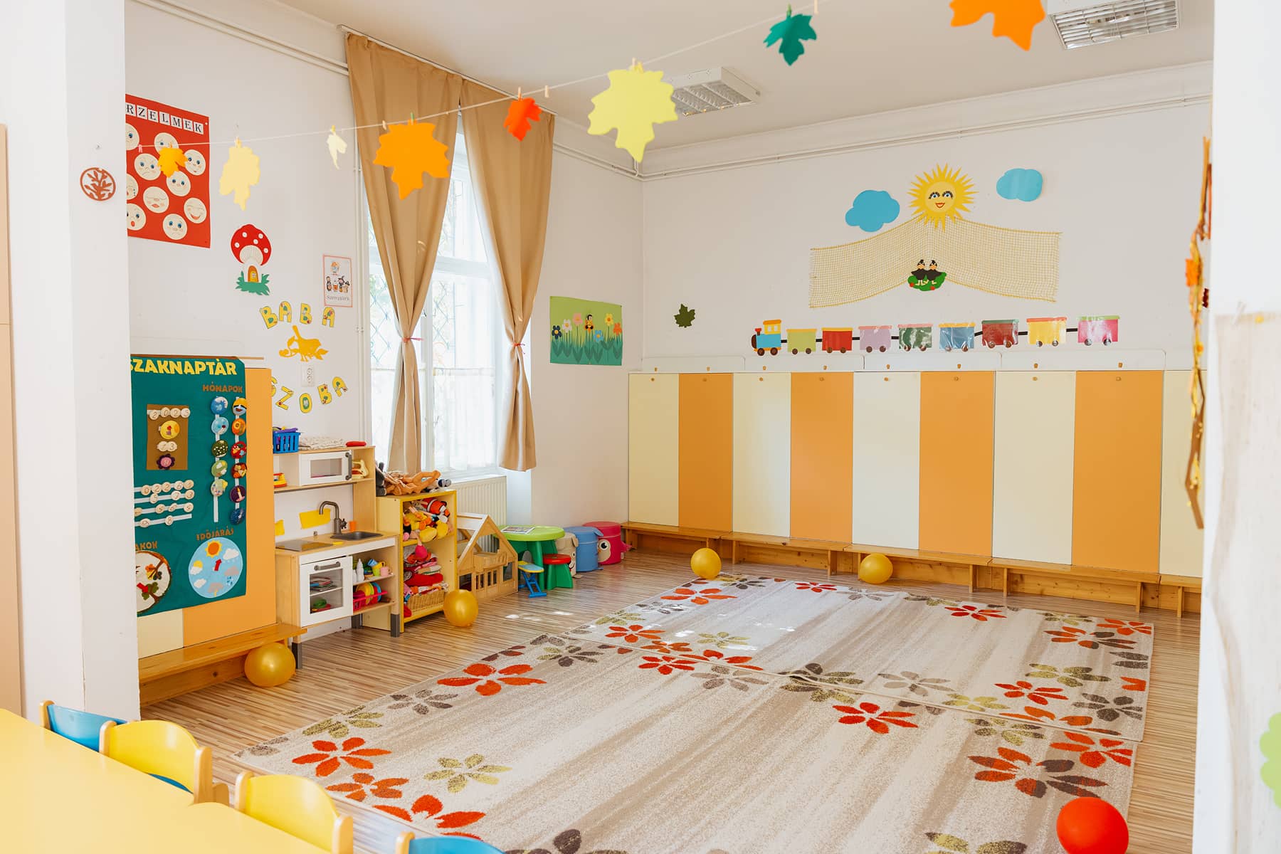 Egy óvodai csoportszoba őszi dekorációval, játékokkal és színes tárolókkal.