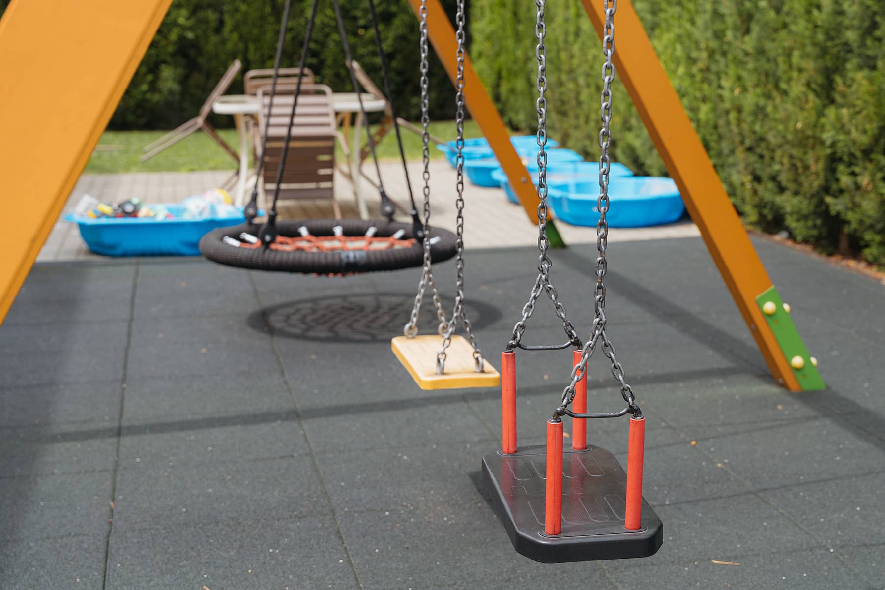 Hinták az óvodai játszótéren, háttérben kék homokozókkal és kerti bútorokkal.