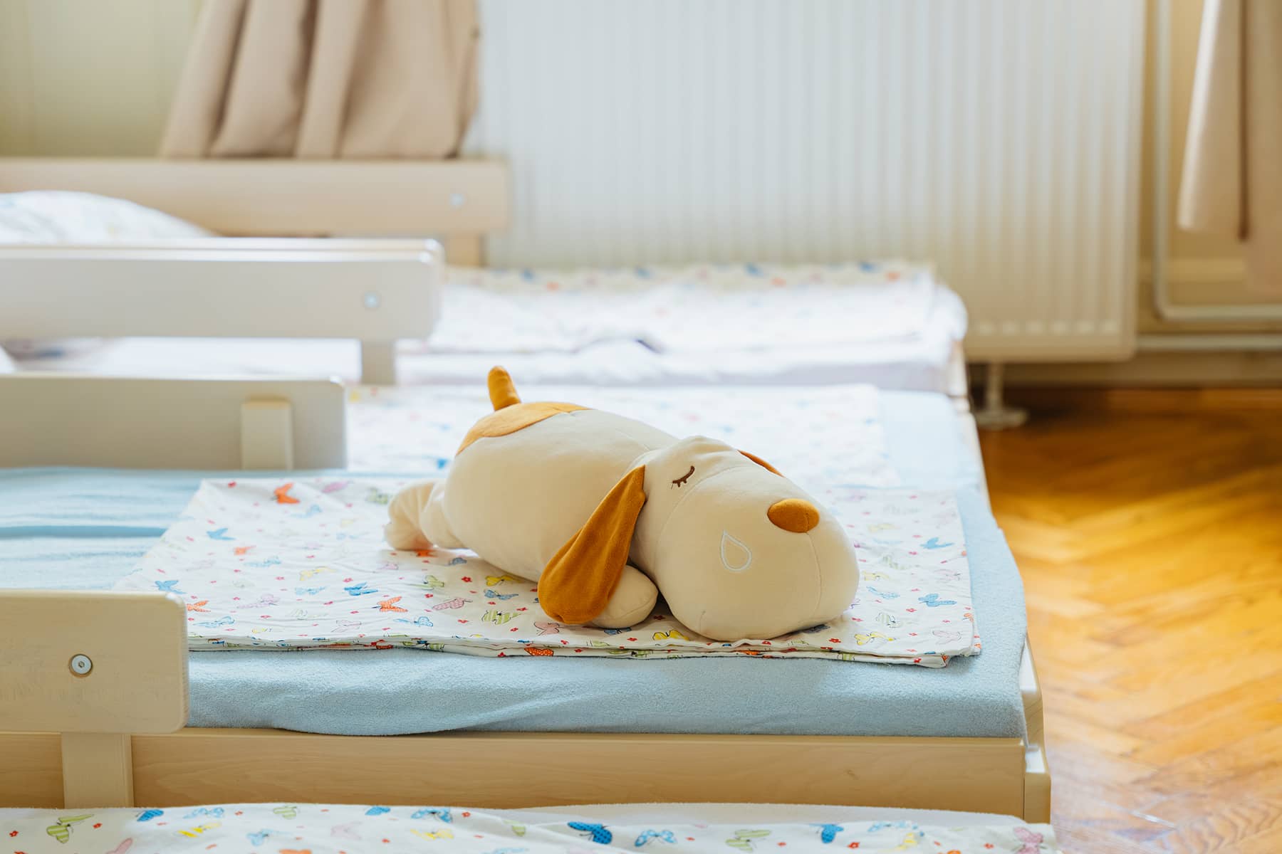 Óvodai pihenőszoba kiságyakkal és plüssjátékkal.