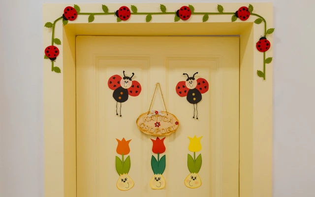 Katica csoport ajtódísz piros katicabogarakkal és színes virágokkal, sárga ajtón elhelyezve