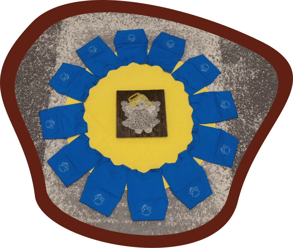 Az Angyalka csoport kék kötényei körben elhelyezve egy sárga kendőn, középen egy angyal formájú fonalkép