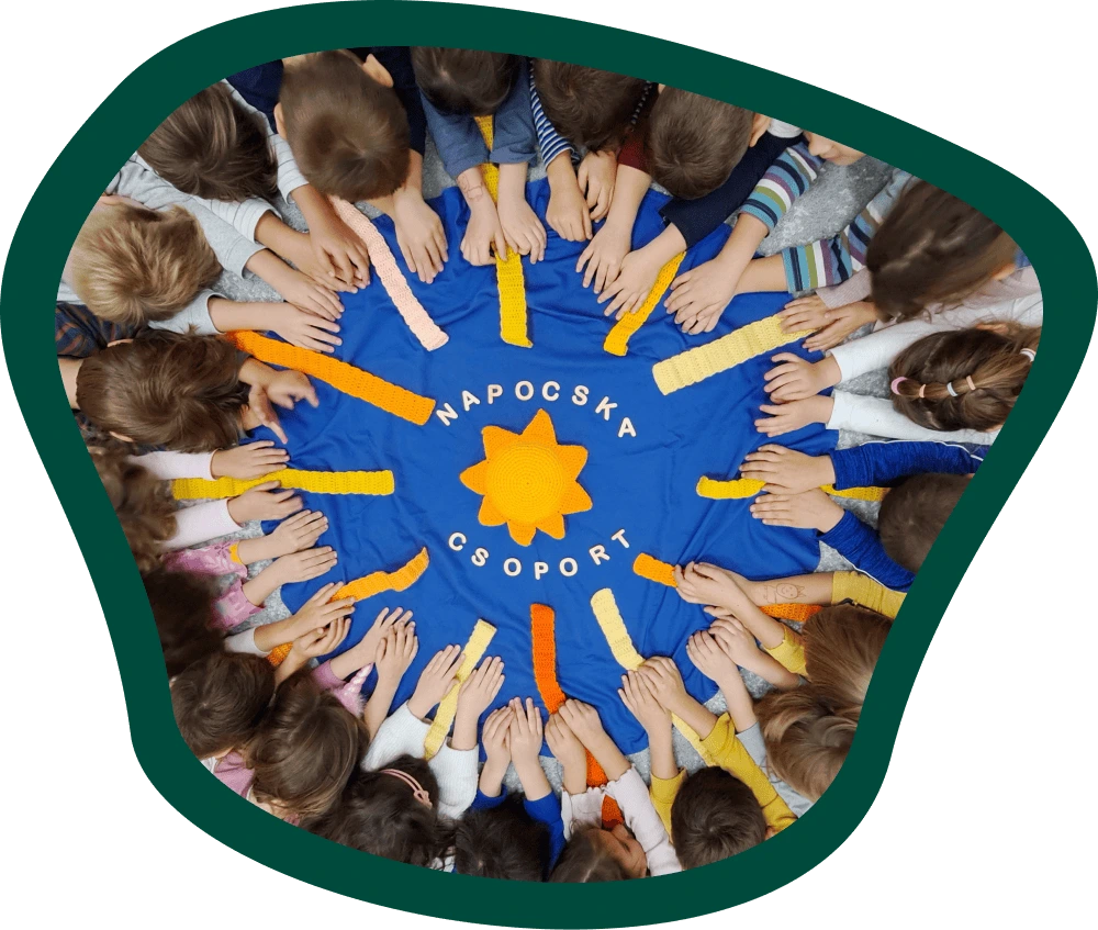 A Napocska csoport gyermekei körben ülnek egy kék kendő körül, amelyen sárga napmotívum és a csoport neve látható