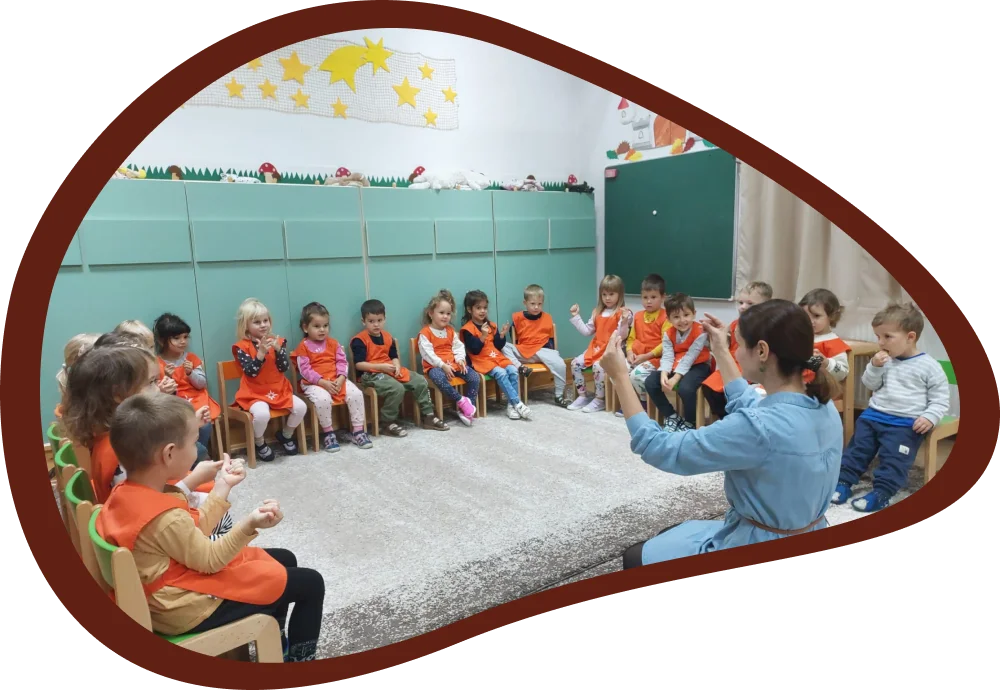 A gyógypedagógus csoportos fejlesztő foglalkozást tart a gyermekeknek, akik körben ülnek és játékos feladatokban vesznek részt.