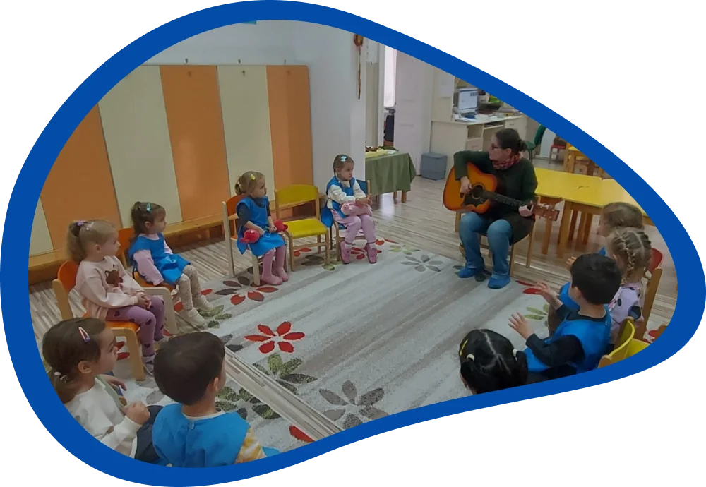 Körben ülő óvodások gitárkísérettel énekelnek és tapsolnak, Kingrica vezetésével, a csoportszobában.
