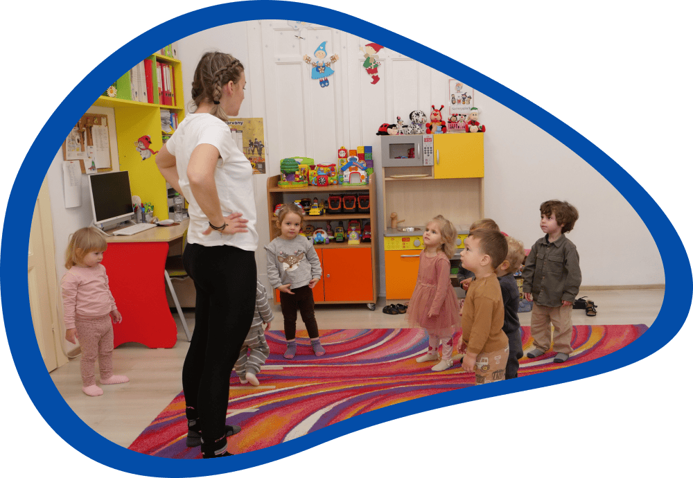 Copiii stau în cerc și urmăresc cadrul didactic în timpul activității motrice, în creșă.