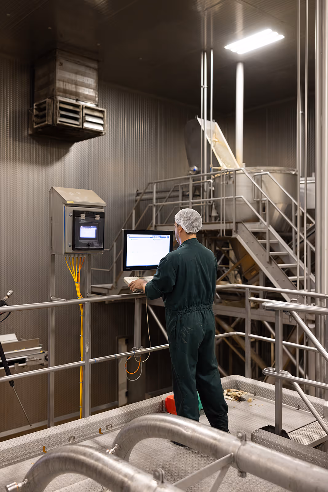 Medewerker in groene overall en haarnetje werkt op een computer in een industriële voedselverwerkingsfaciliteit.