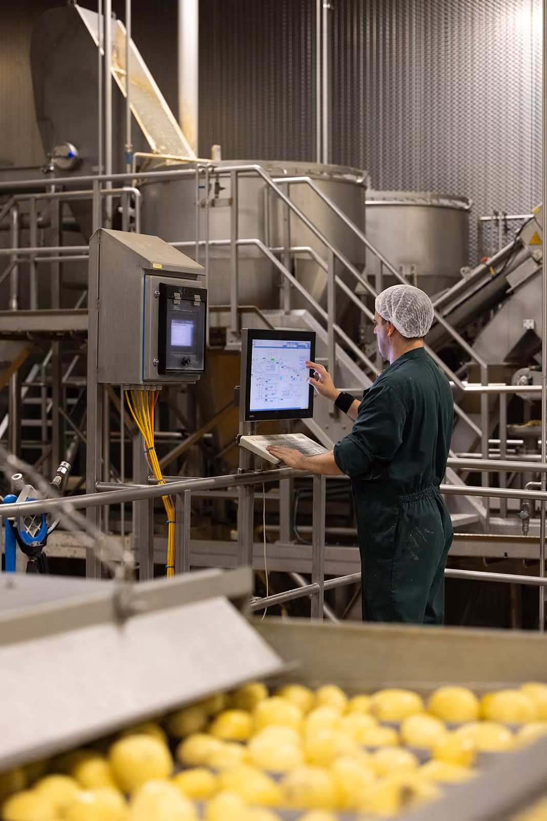Werknemer met haarnetje die een scherm bedient in een fabriek waar aardappelen worden verwerkt.