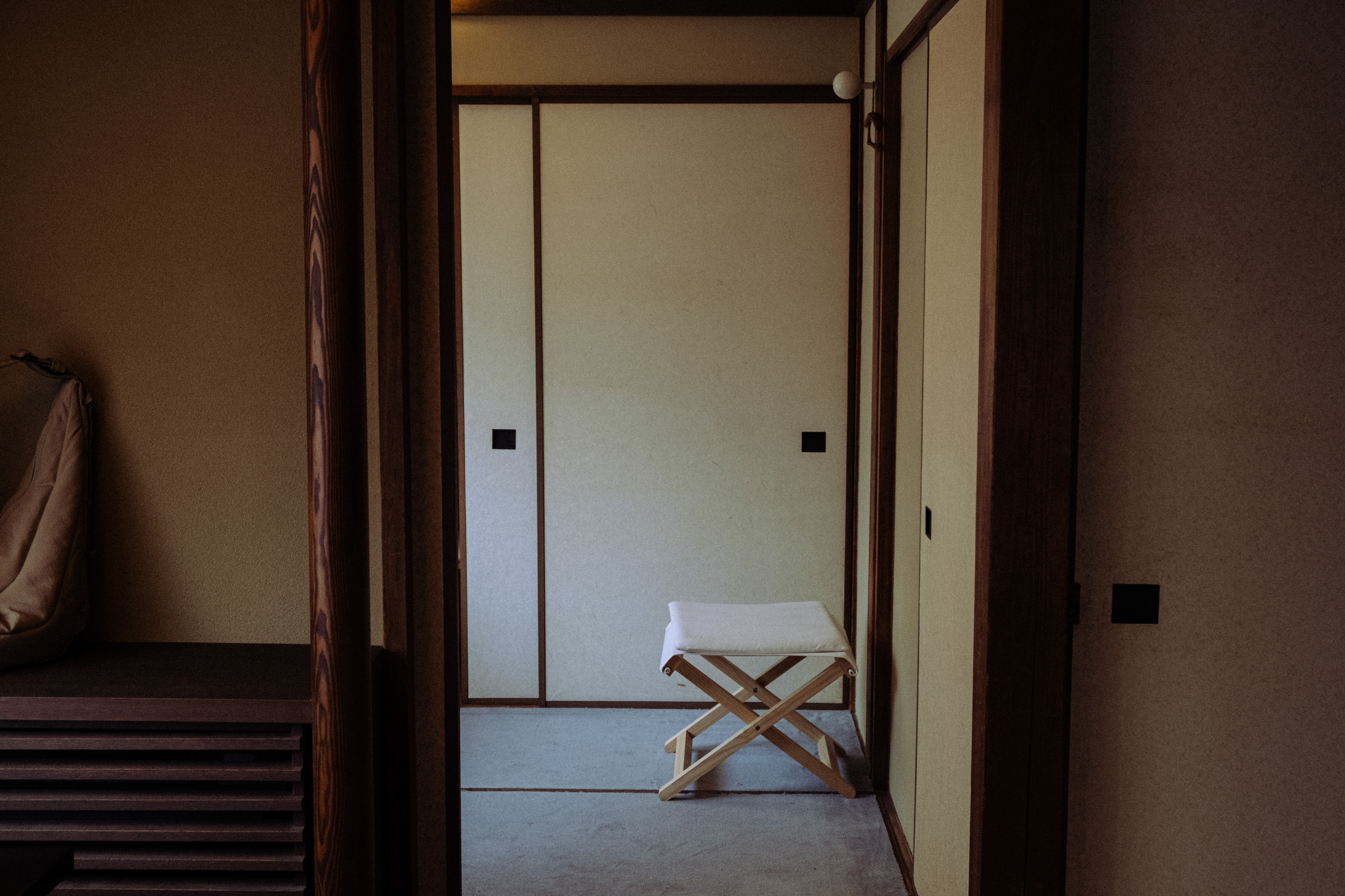 Minimalist room with a small wooden stool with a white cushion against a wall with sliding doors.