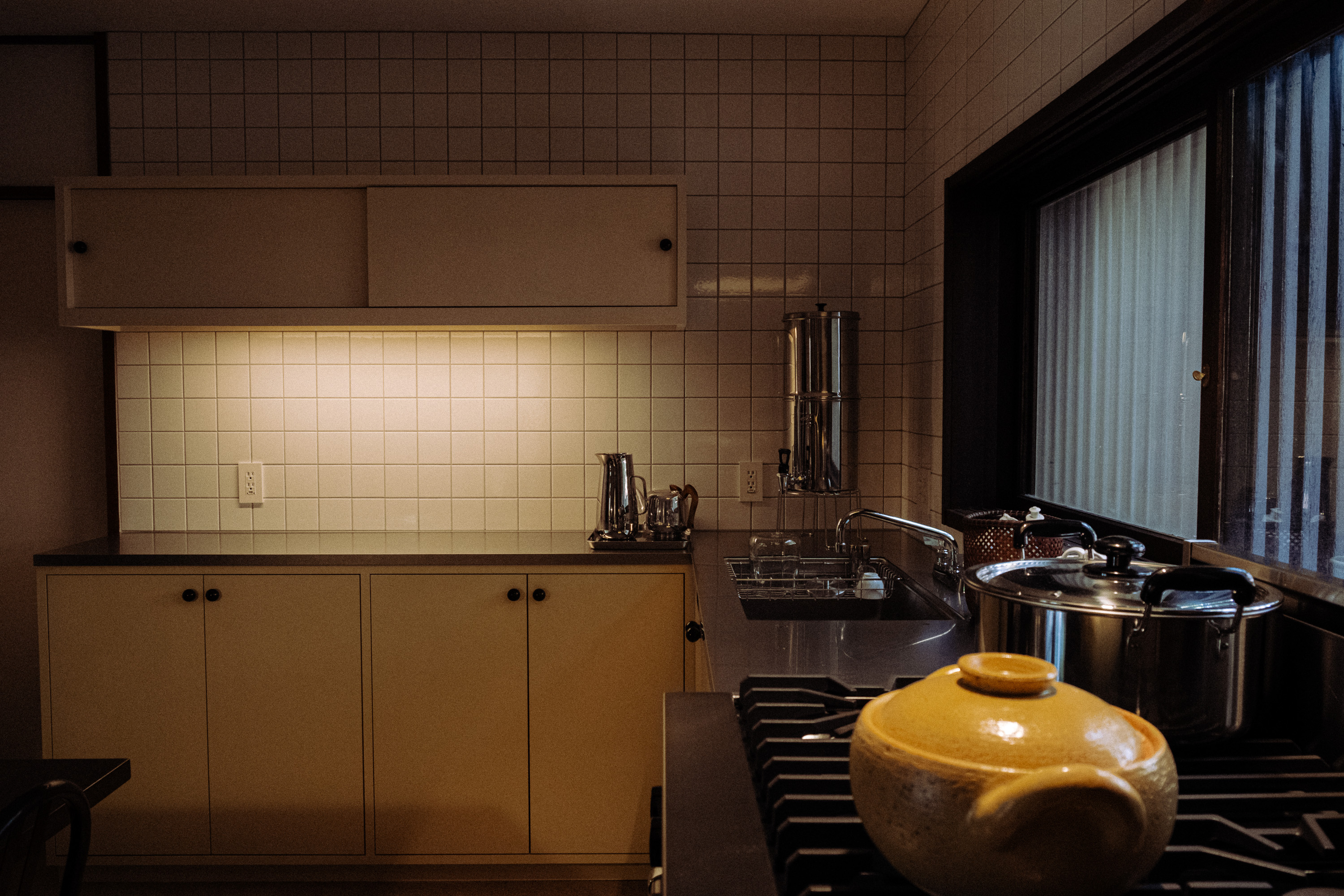 Cozy kitchen corner with yellow cabinets, stainless steel countertop, a yellow pot on the stove, and a large window.