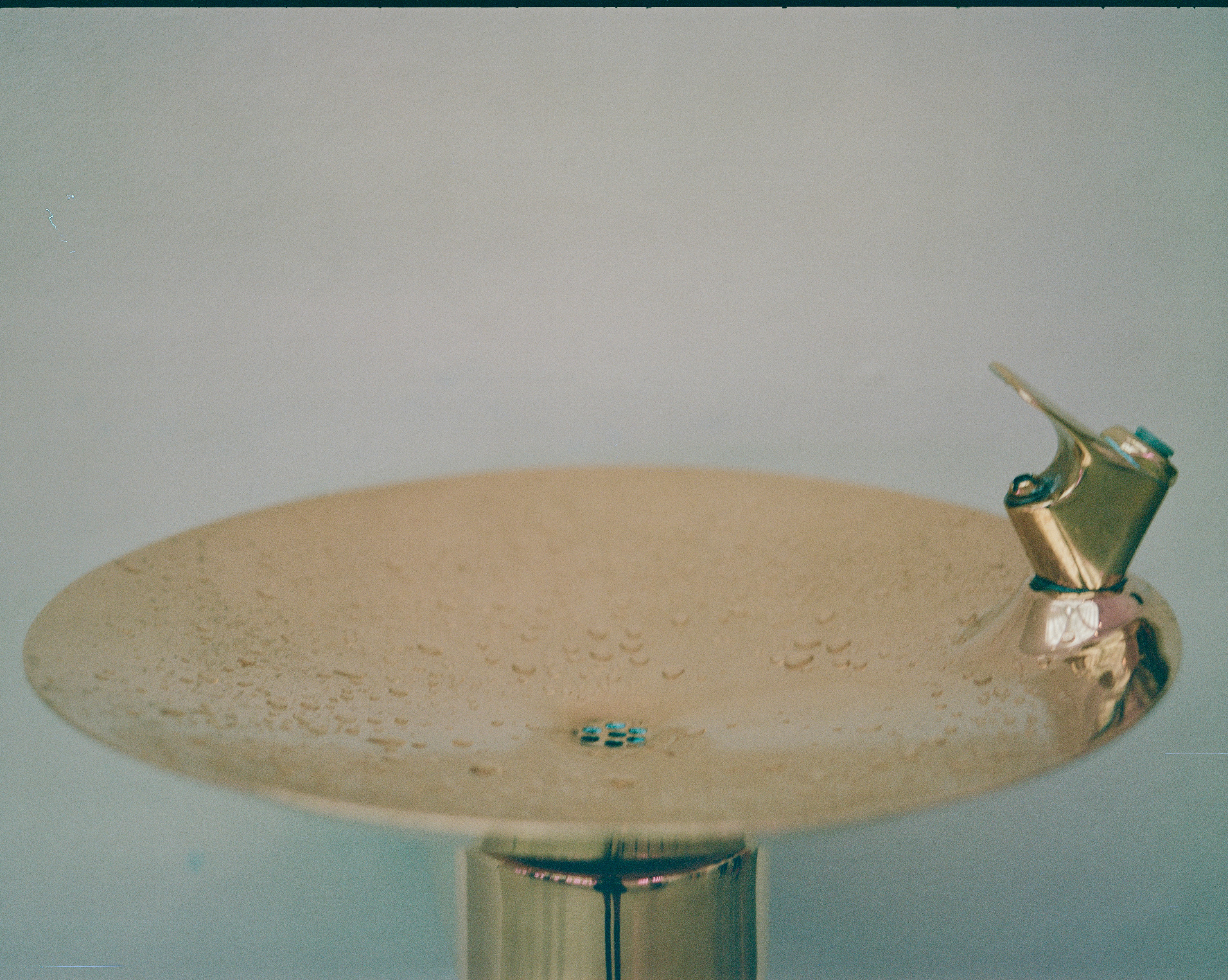 Close-up of a shiny, gold-colored water fountain with water droplets on its basin.