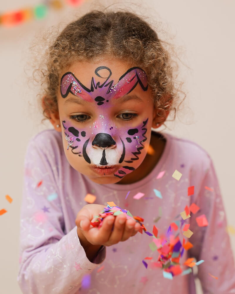 Een foto van een geschminkt meisje die confetti uit haar hand blaast.
