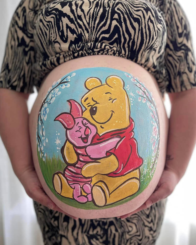 Een foto van een zwangere buik met daarop een afbeelding geschminkt van Knorretje en Winnie de Poeh.
