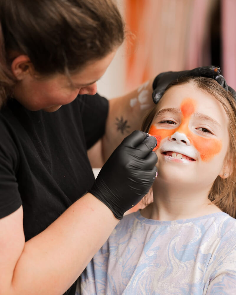 Foto van Luttimutti die een konijngezicht schminkt bij een meisje.