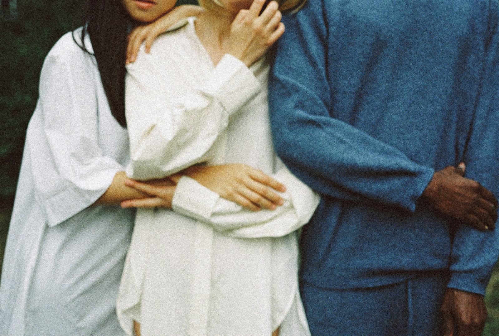 Close-up of three people standing side by side with arms intertwined, wearing casual white and blue clothing.