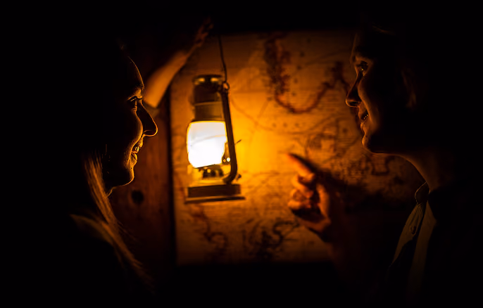 Two people study an old map lit by lantern light