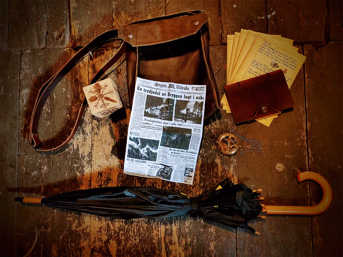 A leather satchle, old newspaper, umbrella and other items lie on an old wooden floor
