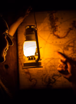 Two people study an old map lit by lantern light