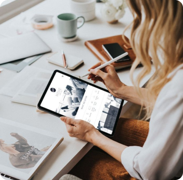 Person holding a tablet with a stylus, interacting with a website interface at a cluttered white desk.