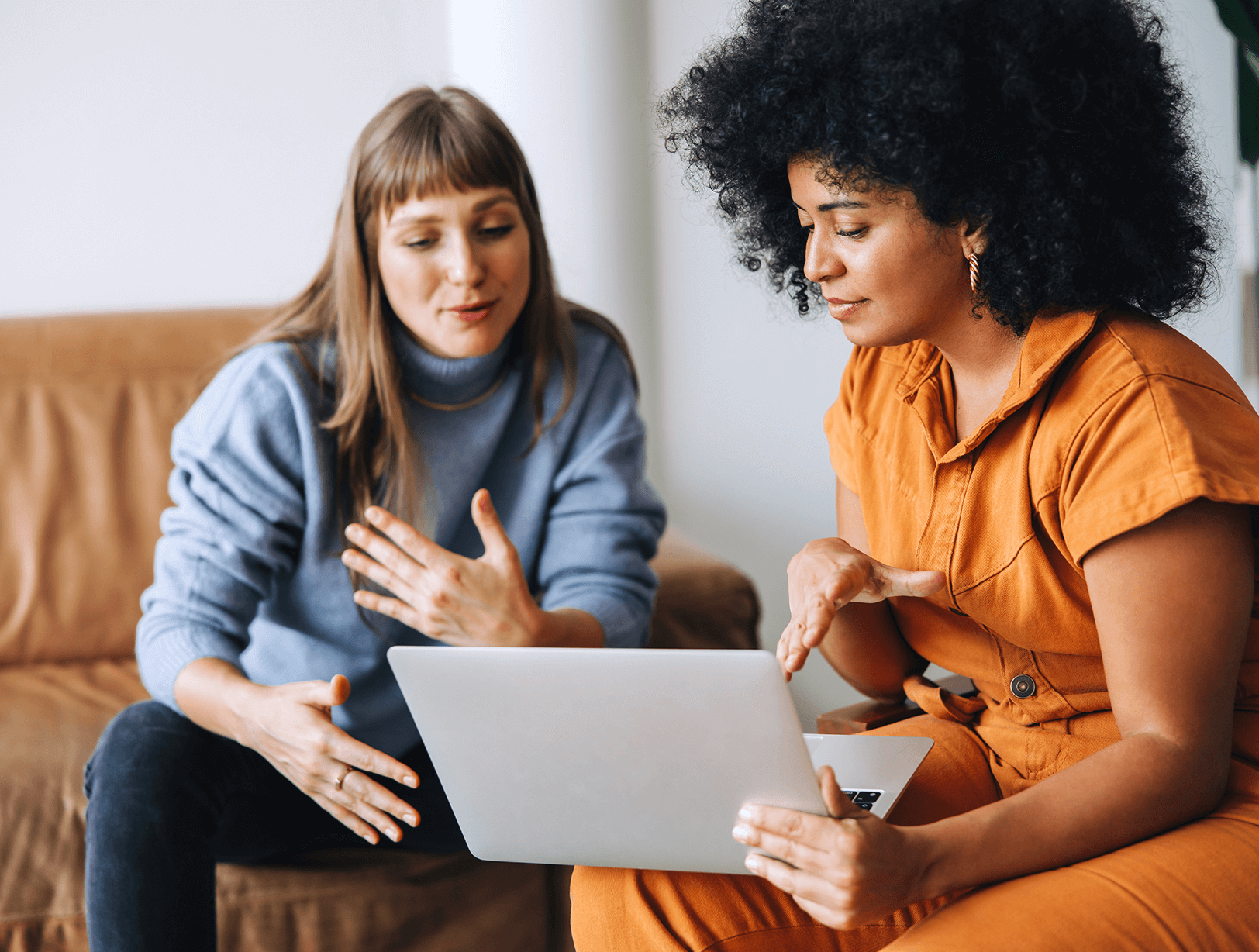 Two women sitting on a couch and chair, engaged in a discussion while looking at a laptop screen.