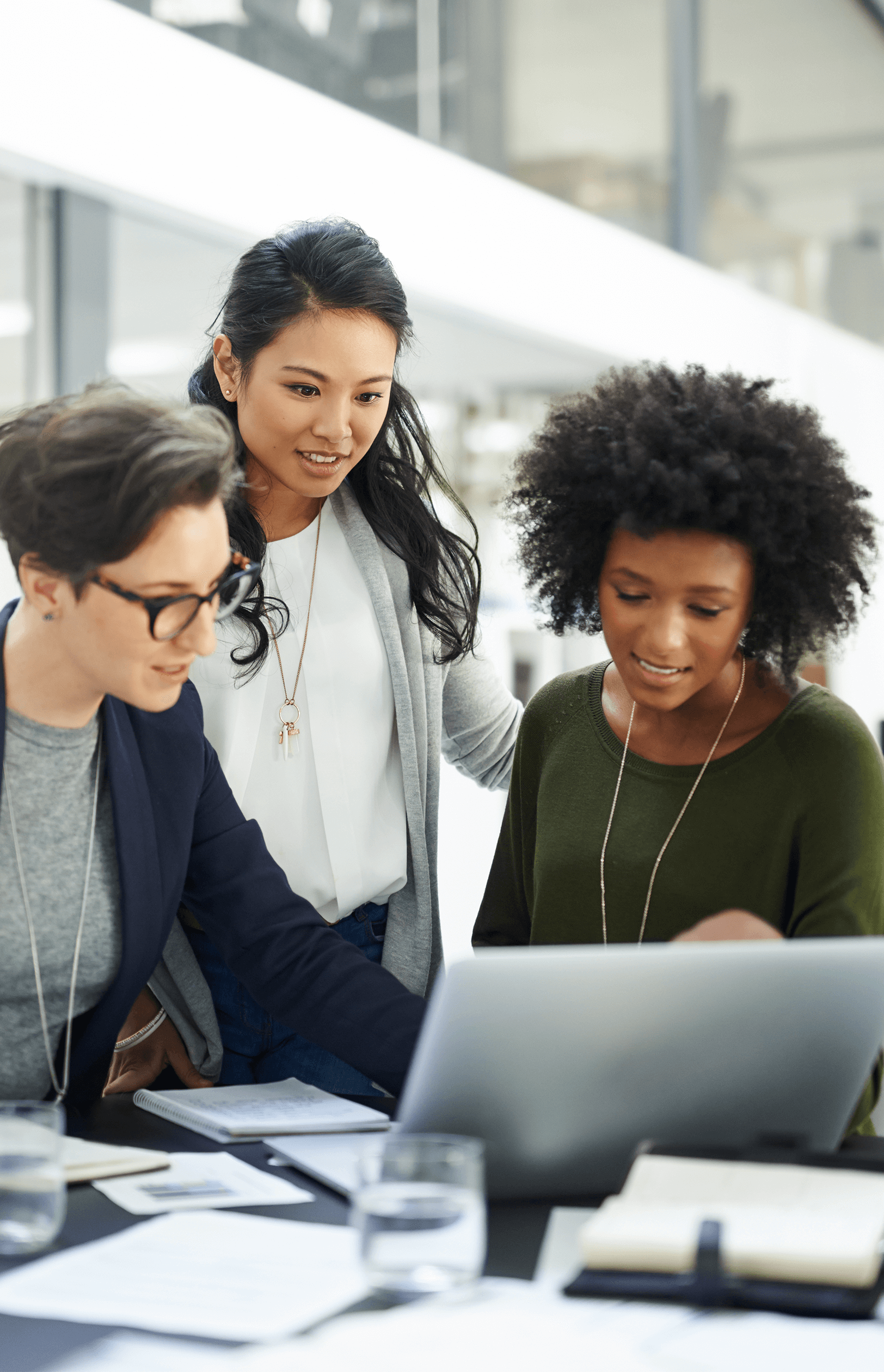 Three diverse women collaborating while looking at a laptop in a modern office.