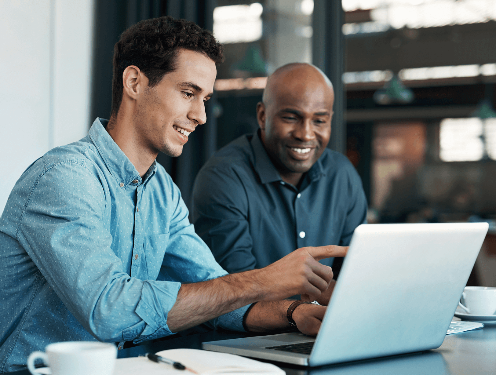 Two men smiling and looking at a laptop together in a modern office setting.