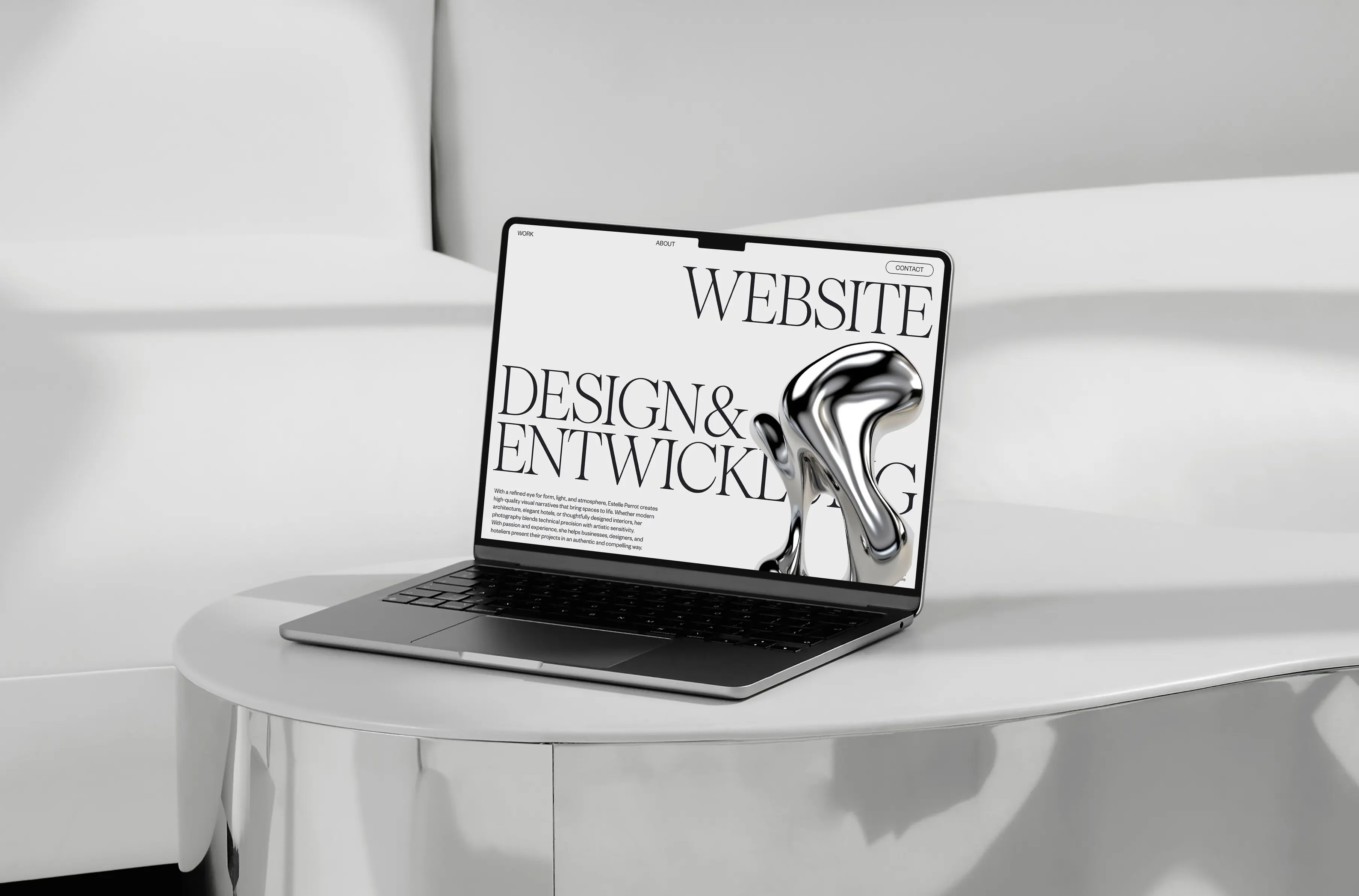 Offener Laptop auf einem weißen, geschwungenen Tisch, auf dem eine Website-Designseite mit großem Text und einer glänzenden abstrakten 3D-Form angezeigt wird.