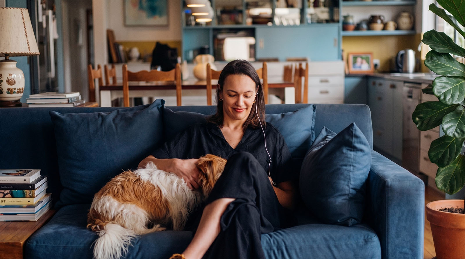 Woman sitting on blue couch petting a small brown and white dog using her yōjō VNS device