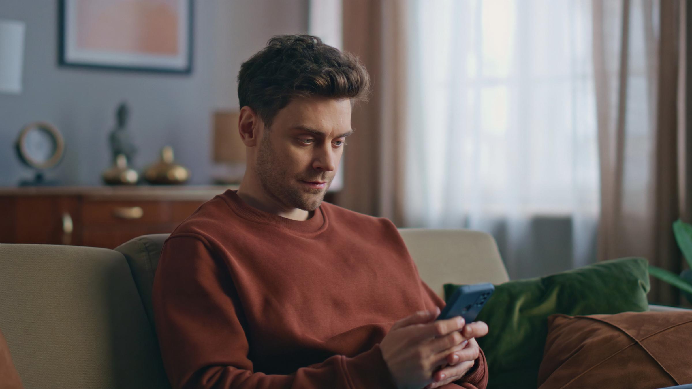 Man in rust-colored sweater sitting on a couch, having a conversation with their coach on the yōjō app.