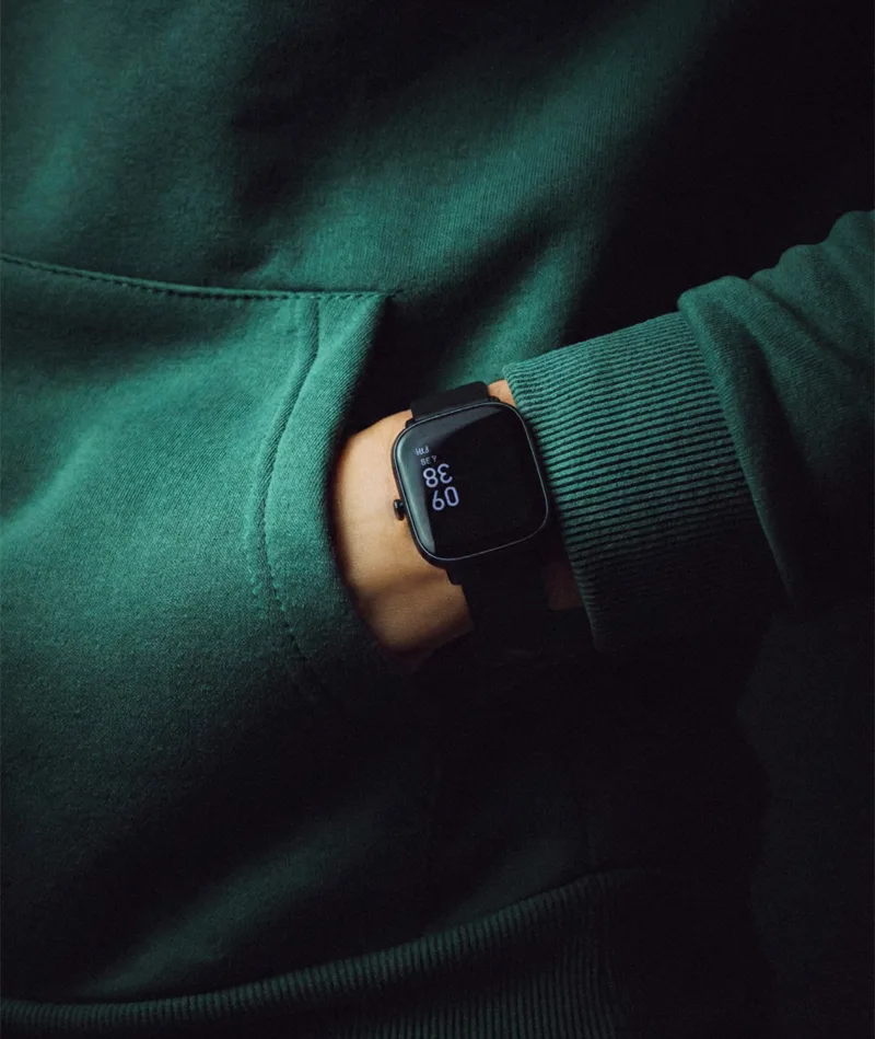 Person wearing dark green sweatshirt with hand in pocket and black smartwatch.