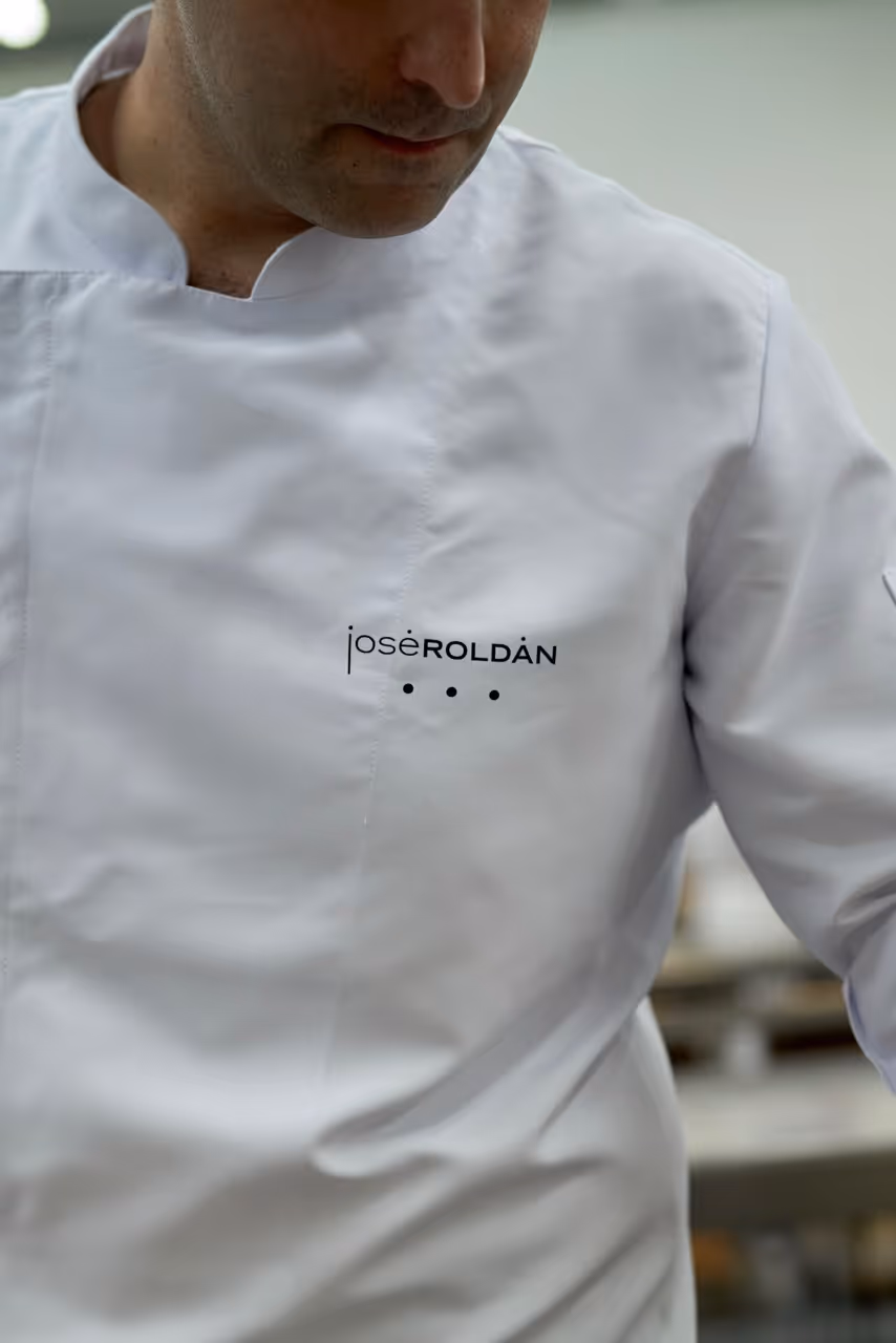 Plano cercano de un chef con chaqueta blanca bordada con el nombre José Roldán.