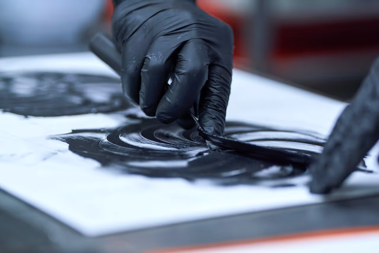 Mano con guante negro extendiendo chocolate con una espátula sobre una superficie blanca.