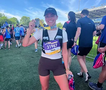 Smiling female runner holding a finisher medal and a water bottle on a sports field after a race event.