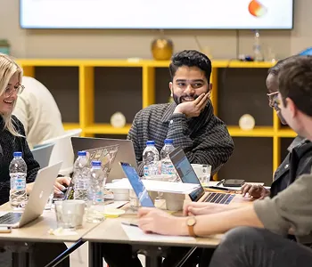Group of young professionals collaborating around a table with laptops and water bottles in a modern office setting.