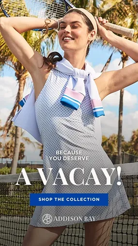 Smiling woman in a sleeveless dress and headband holding a tennis racket behind her head on a sunny outdoor tennis court with palm trees.