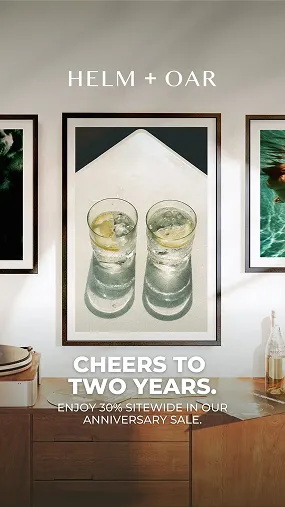 Two glasses of ice water with lemon slices on a tray, framed and hung on a wall above a wooden cabinet with bottles and decor.