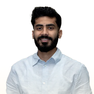 Man with dark hair and beard wearing a light blue button-up shirt smiling against a plain background.