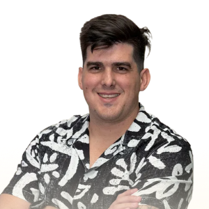 Smiling man with short dark hair wearing a black and white patterned shirt with folded arms.