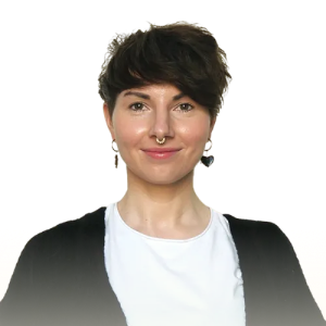 Smiling woman with short dark hair, wearing a white shirt and black cardigan, and a septum piercing.