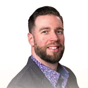 Smiling man with short dark hair, beard, and mustache wearing a dark blazer over a purple floral shirt.