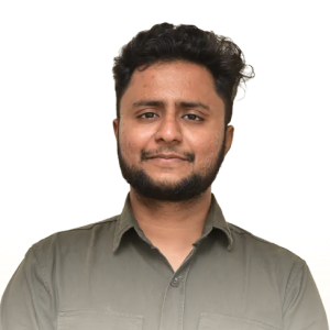 Man with short curly hair and beard wearing an olive green button-up shirt, smiling slightly with arms crossed.