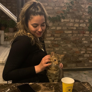 Young woman in black holding and petting a tabby cat in a cozy indoor setting with a brick wall background.